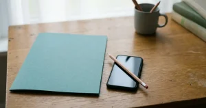 Ein geschlossenes Dokumentenmäppchen neben einem Smartphone und einem Stift auf einem Tisch.